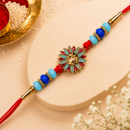 A red thread bracelet with a gold Ganesh charm, blue and light blue beads, and gold accents, on a light cream surface with