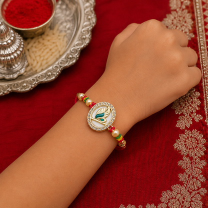 A child's arm wears a golden Mor Pankh design with American diamonds and pearls on a red thread, over a red embroidered