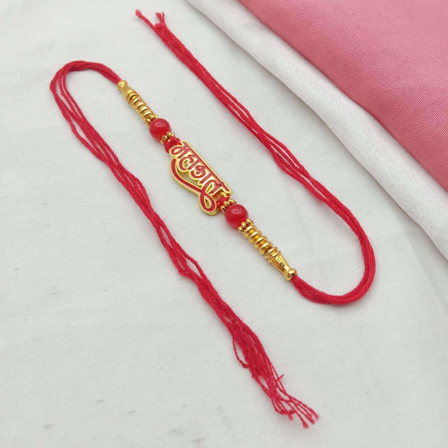 A red thread with a gold and red Mahakal calligraphy charm, red beads, and gold accents is laid out on a white surface with