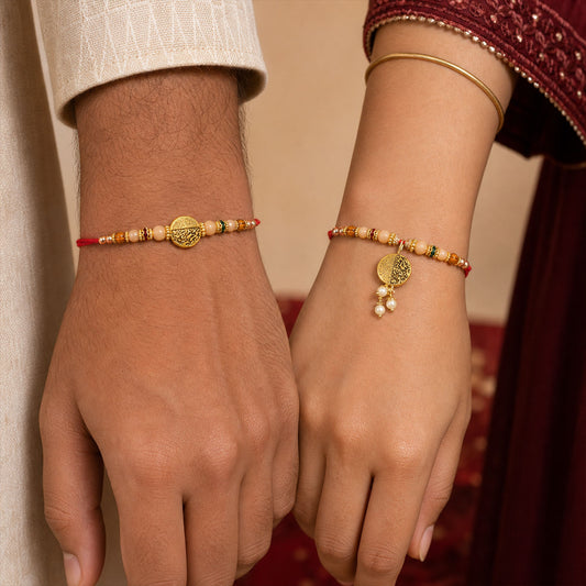 Two hands are shown wearing matching red thread bracelets with gold medallions and peach, brown, and green beads.