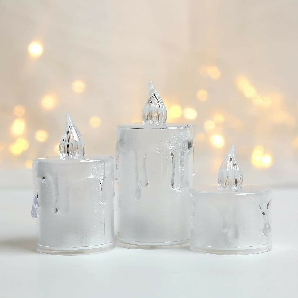 Three clear plastic LED candles, unlit, stand on a white surface with a soft, out-of-focus background.
