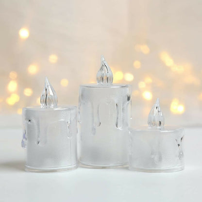Three clear plastic LED candles, unlit, stand on a white surface with a soft, out-of-focus background.