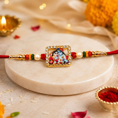 A gold-toned square Radha Krishna enamel charm with a crystal border and pearl accents is centered on a red thread with