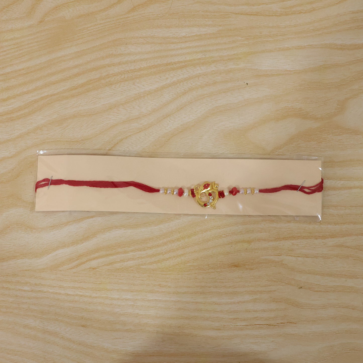 Golden Om Rakhi with Red Beads and Pearl Dotted Thread