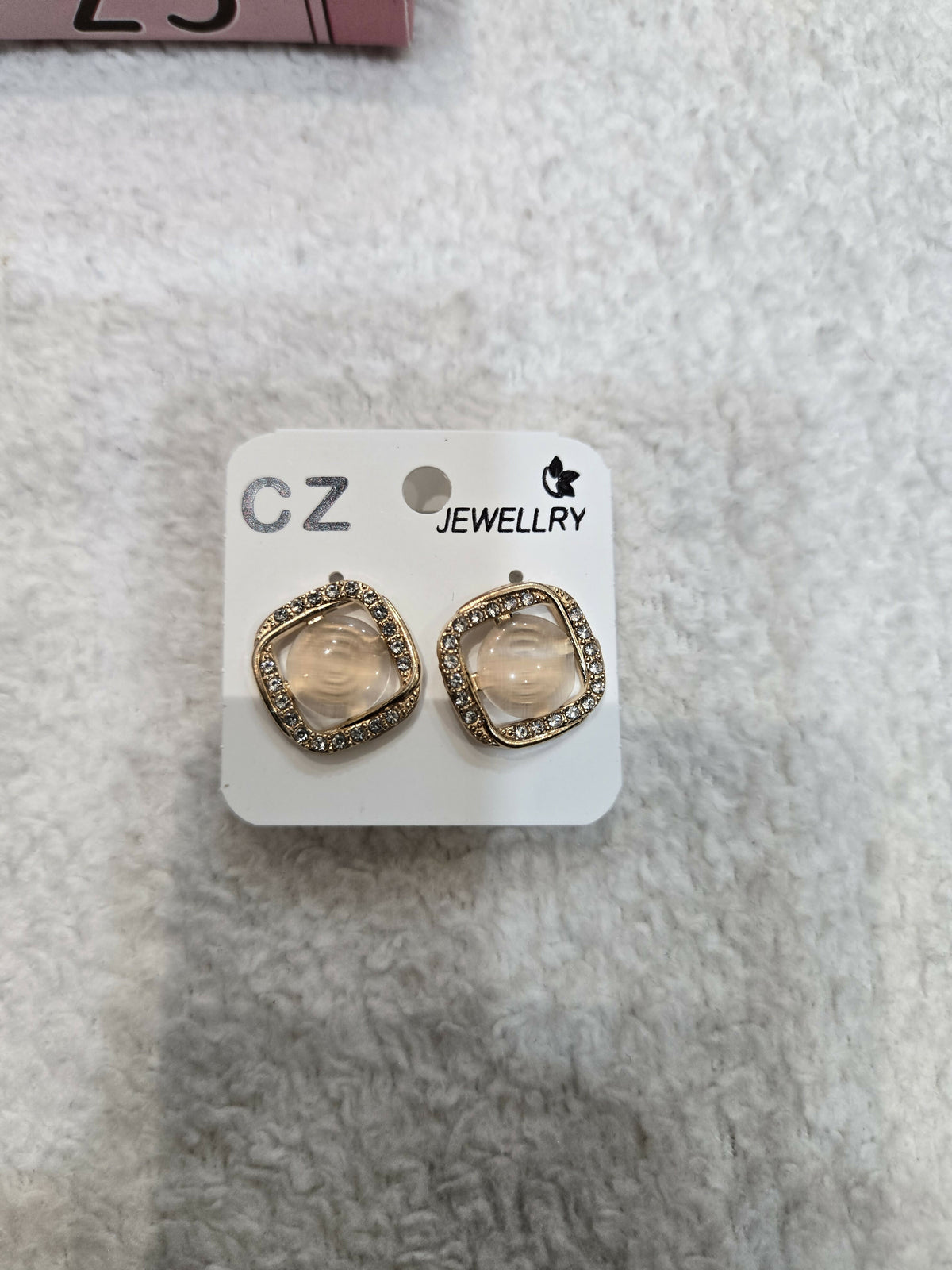 A pair of square stud earrings with clear stones and sparkling borders is presented on a white jewelry card.