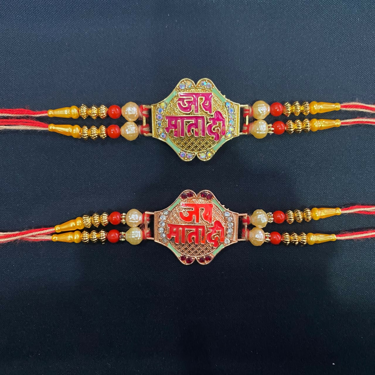 Two decorative bracelets, one green and one red, with "Jai Mata Di" written in Hindi, adorned with pearls and beads on a