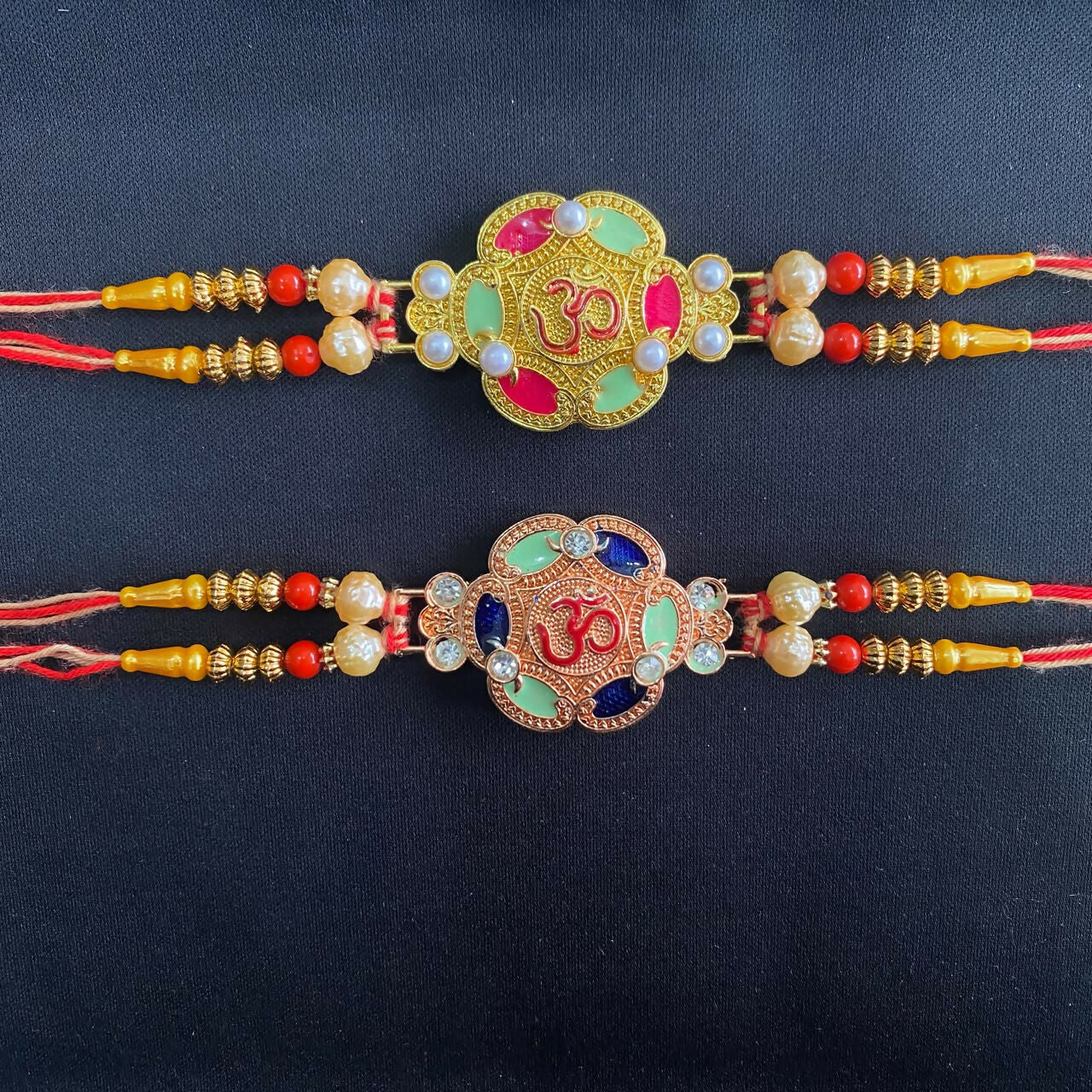 Two gold and rose gold Om bracelets, one with pink and green enamel, the other with blue and green, on a plain black