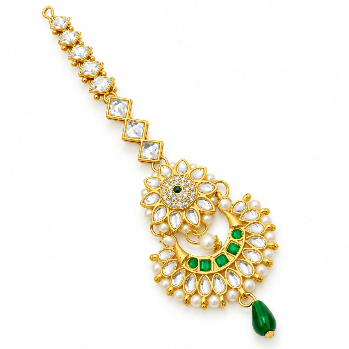 A gold-tone maang tikka with clear kundan stones, green gems, and small white pearls on a plain white background.
