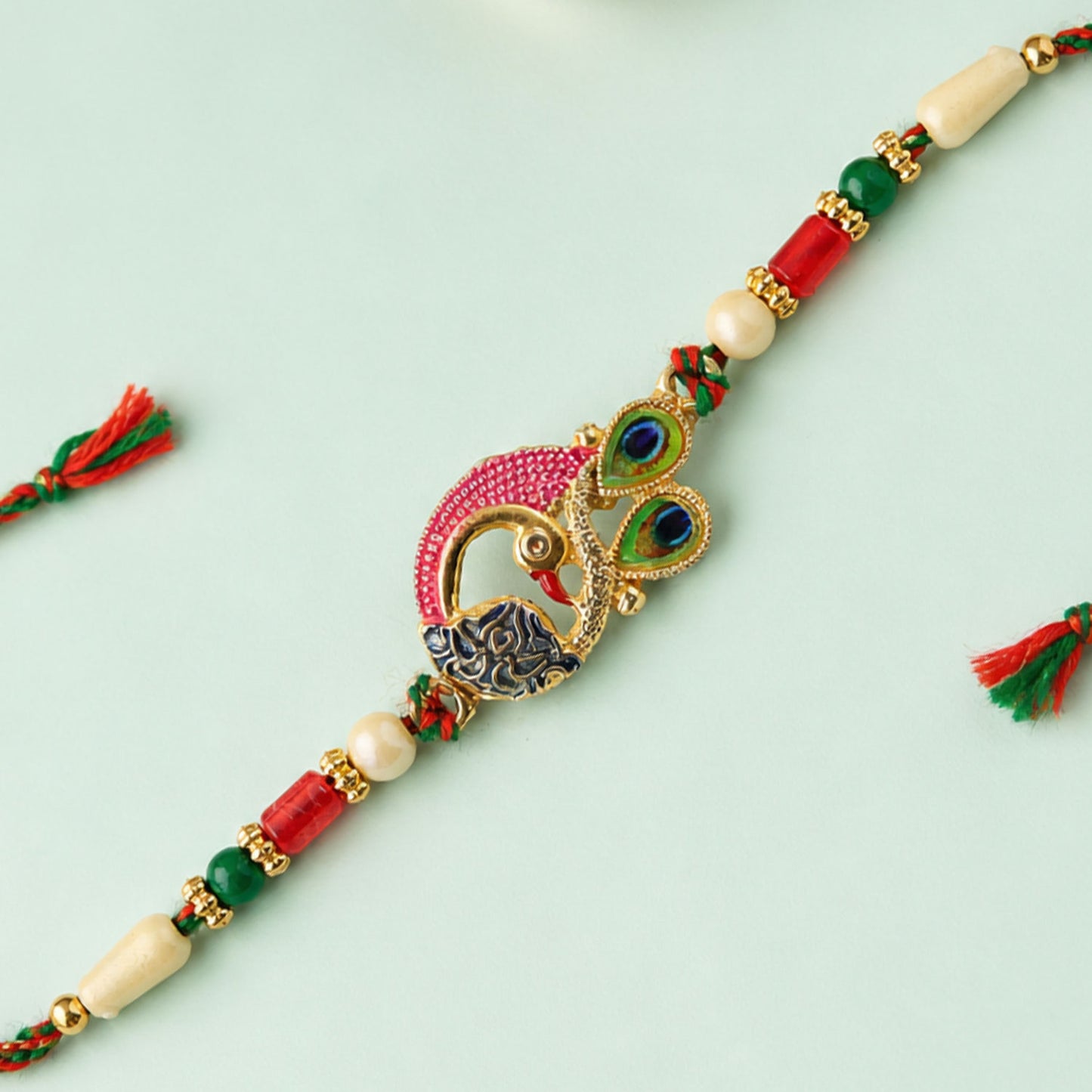 Peacock Rakhi Set with Red Thread, Gold Beads and Meenakari Accent Design