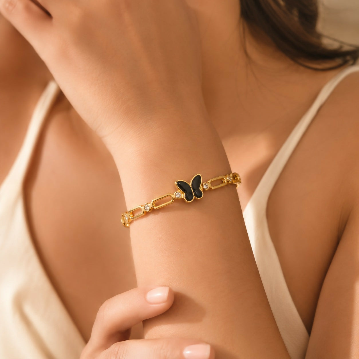 A woman's arm models the gold-tone bracelet with a black butterfly charm and clear crystal accents.
