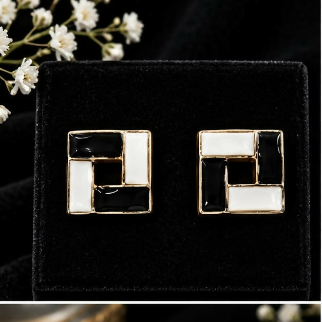 A pair of black and white square earrings with gold accents on a dark velvet surface.