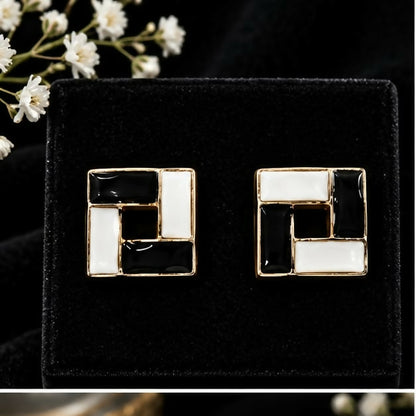 A pair of black and white square earrings with gold accents on a dark velvet surface.