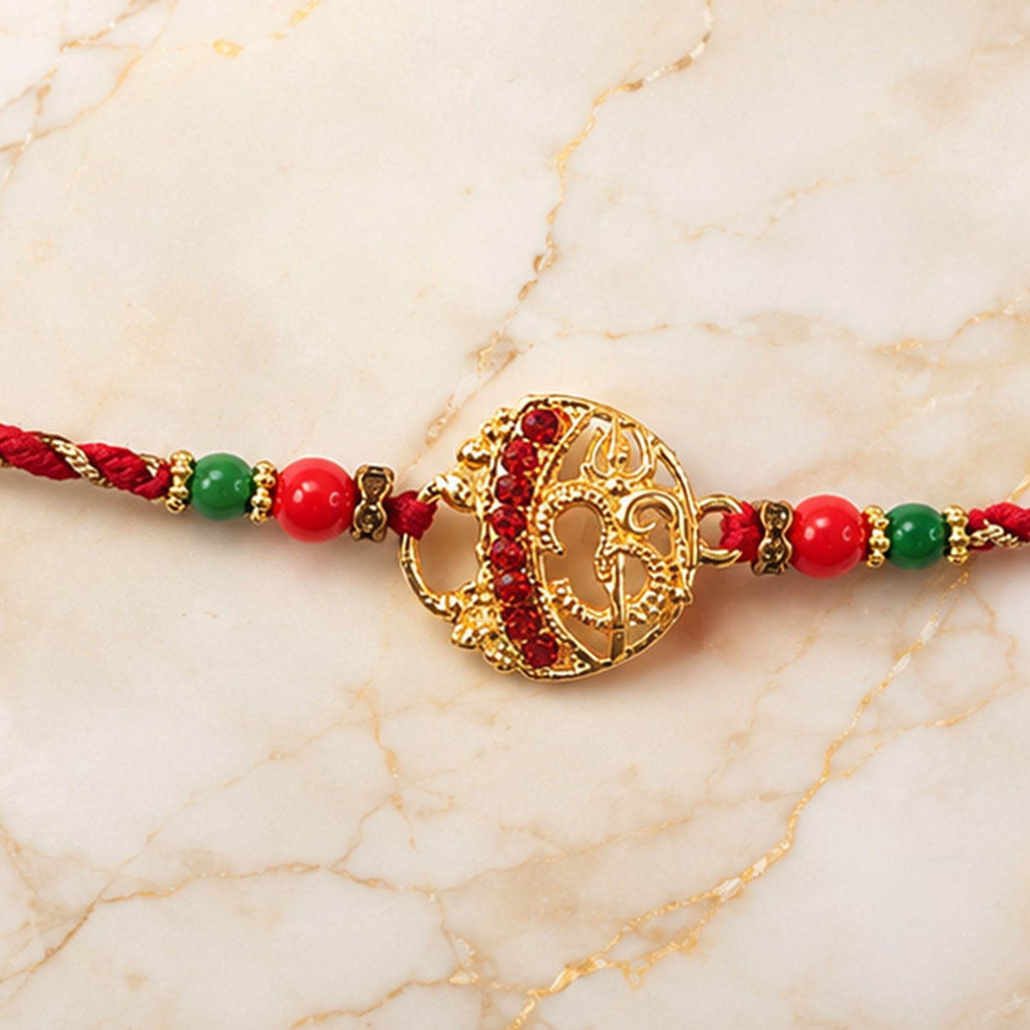 Golden Red Diamond Om Trishul Rakhi with Green Beads and Twisted Thread