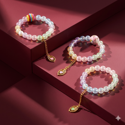 Three pastel beaded bracelets with gold leaf charms on a dark red tiered surface. Each bracelet has a different central bead.