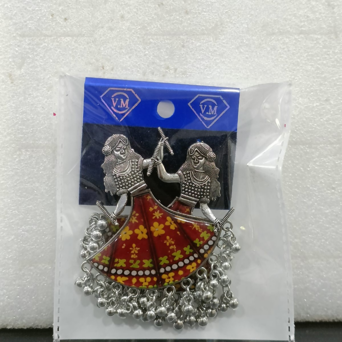 A pair of silver oxidized dancing girl earrings with maroon and yellow skirts, packaged in a clear plastic bag with a blue