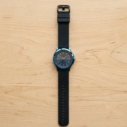 A blue watch with a black strap and golden markers is shown from above on a light wooden surface.