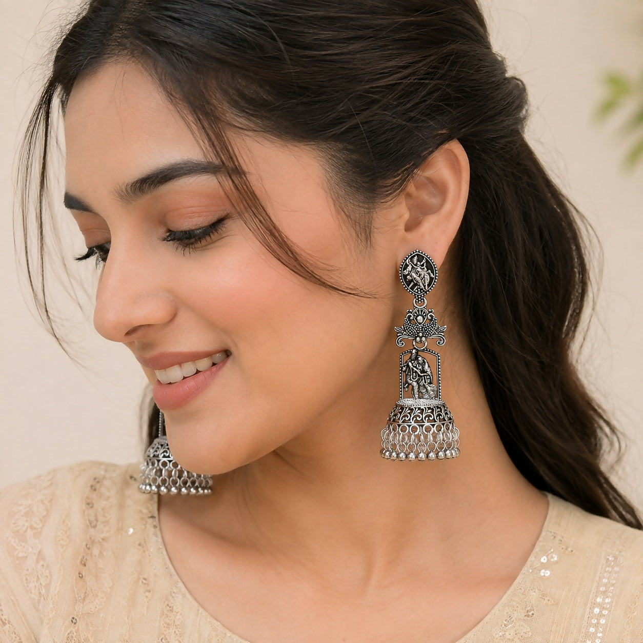 A woman models one of the oxidized silver jhumka earrings, showing the Radha Krishna temple design.