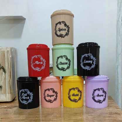 Nine colorful spice containers in black, red, peach, mint, yellow, pink, purple, and gray, arranged in a pyramid on a wooden