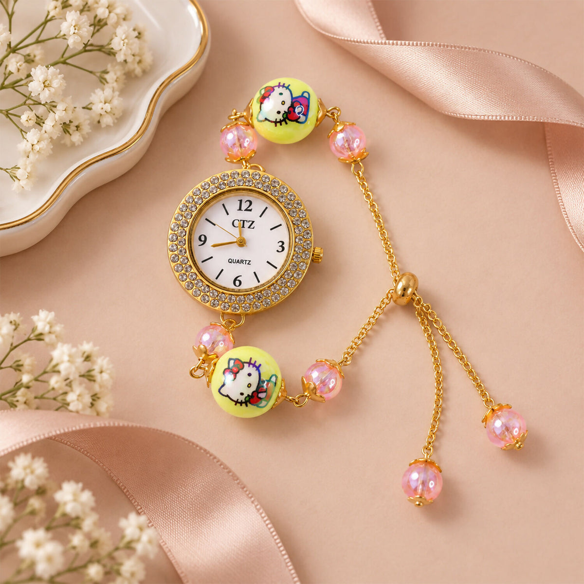 A gold-tone bracelet watch with a rhinestone-trimmed dial, two yellow cartoon character beads, and smaller pink beads, on a