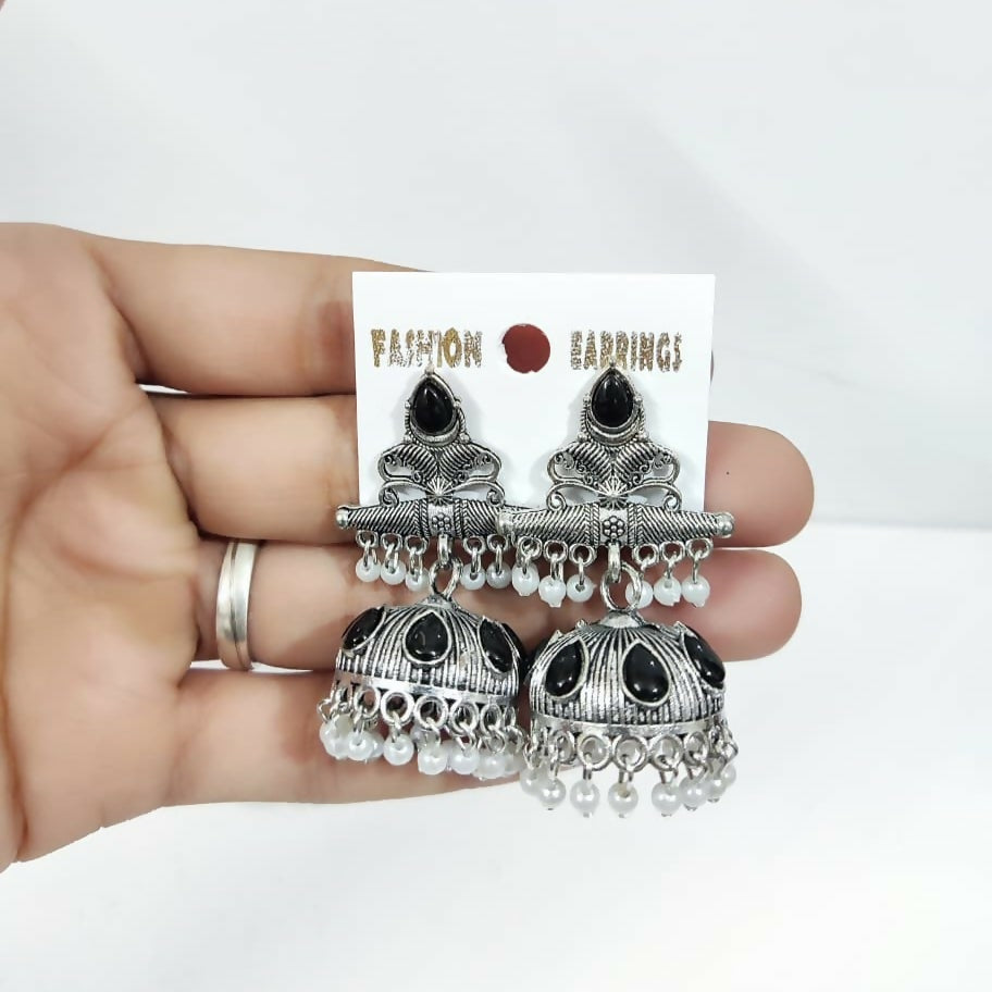 A hand holds the oxidized silver jhumka earrings with black stones and white pearls on white