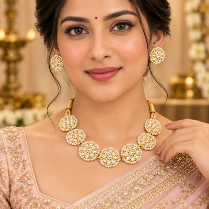 Woman wearing a golden kundan and pearl necklace with matching stud earrings, smiling gently.