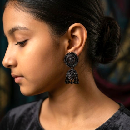 A young person models a single black oxidised jhumka earring, showcasing its intricate design and size.