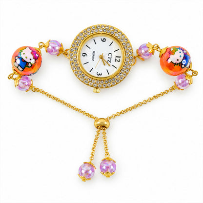 A gold-tone bracelet watch with a rhinestone-bordered dial, two orange cartoon character beads, and smaller purple beads, on