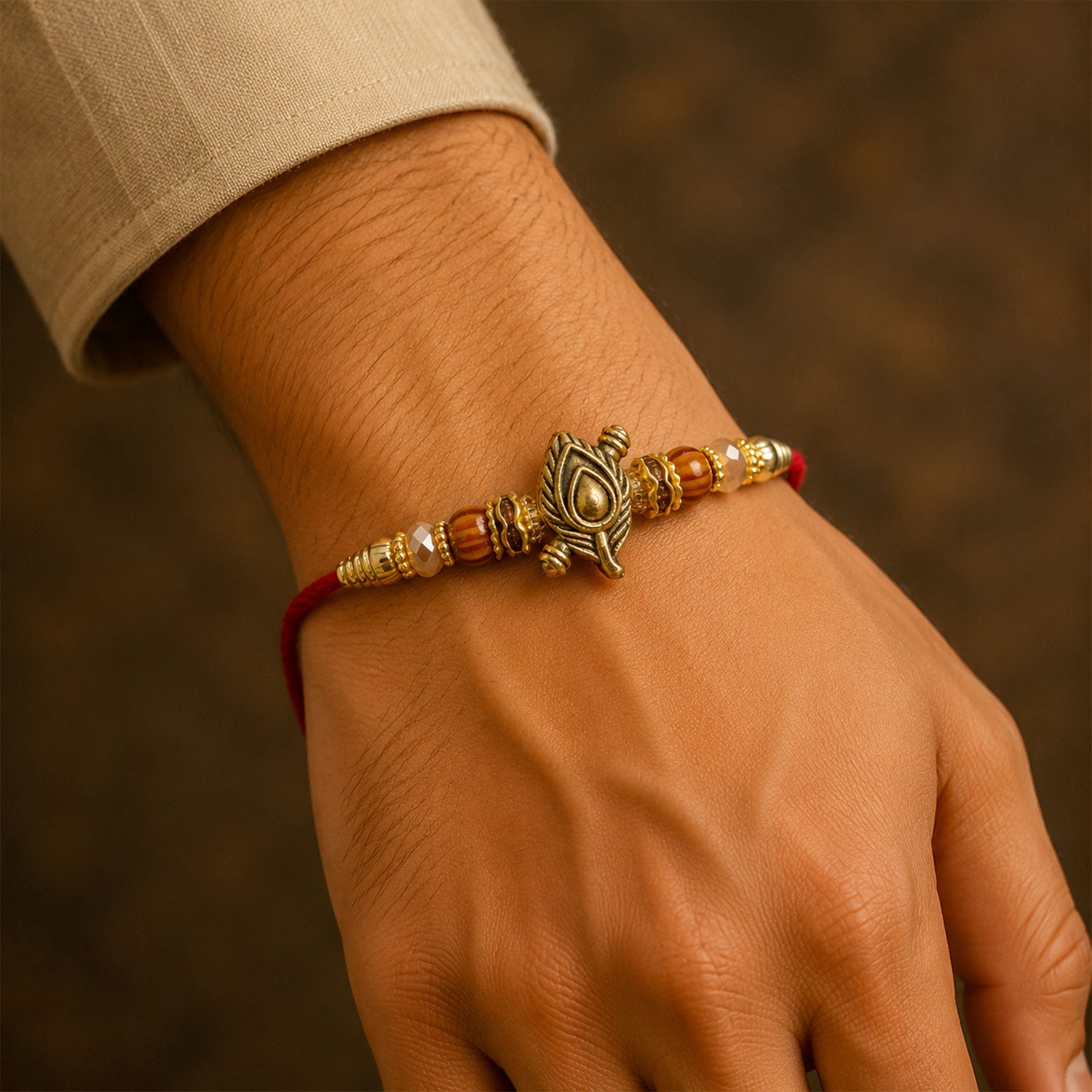 Peacock Paisley Golden Rakhi with Leaf Style Centre, Red Thread and Pearl Accents