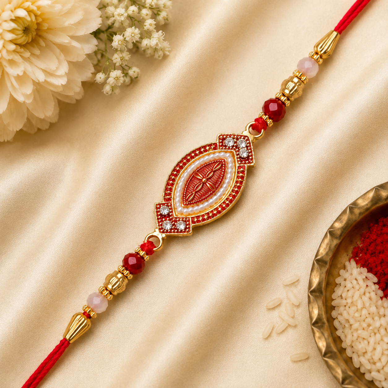A red and gold bracelet with an oval centerpiece, adorned with white beads and red stones, lies on a golden silk cloth with