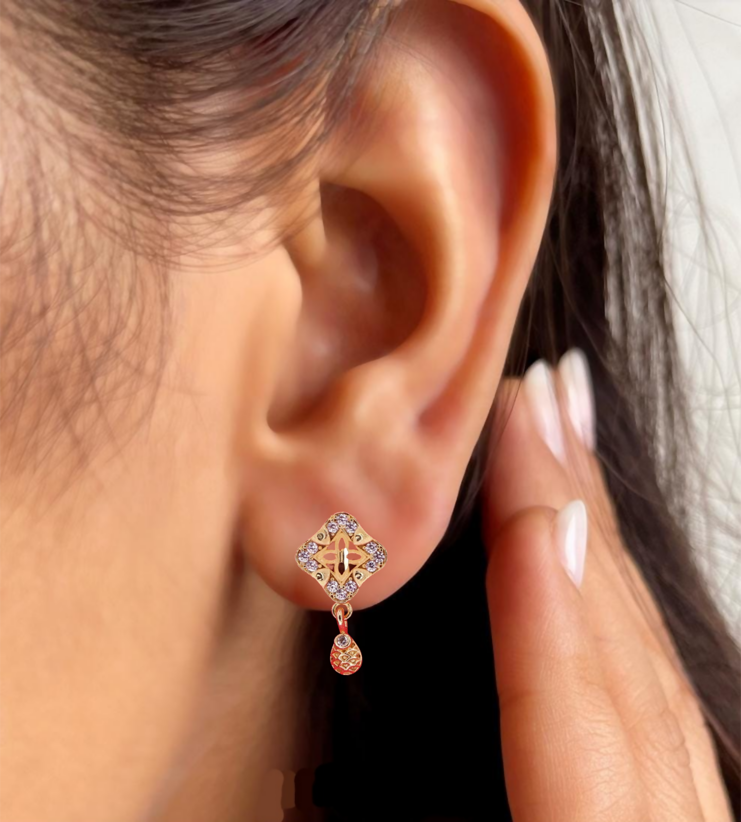 Detailed view of earrings' textured gold-plated droplet with traditional motif