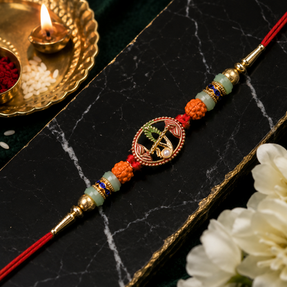 A red and gold bracelet with a central oval charm depicting a flute and peacock feather, surrounded by various colored beads