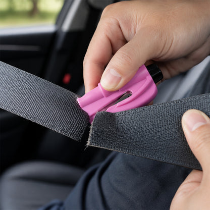 A person's hands demonstrate using the pink emergency tool to cut a gray car seat belt, with the interior of a car visible.