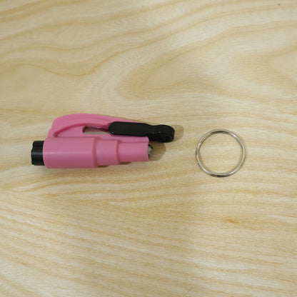 A pink emergency tool with a black clip and a separate silver keychain ring are placed on a light wood grain surface.