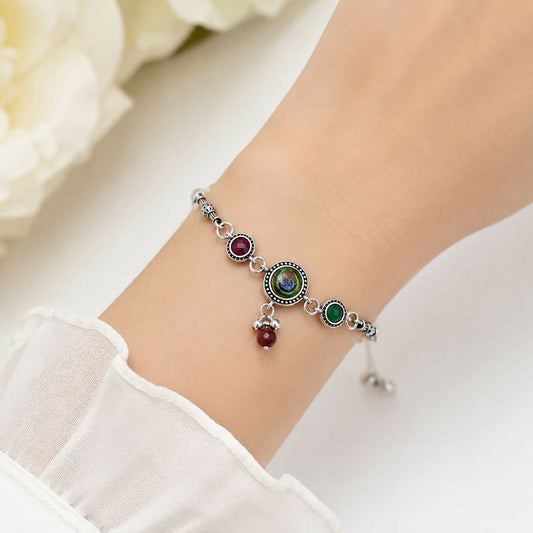 A woman's wrist wears an antique silver adjustable bracelet with a peacock eye cabochon, maroon and green side stones, and