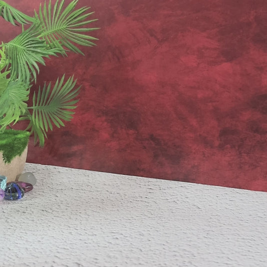 A green potted plant and colorful glass stones sit on a textured white surface against a red wall.