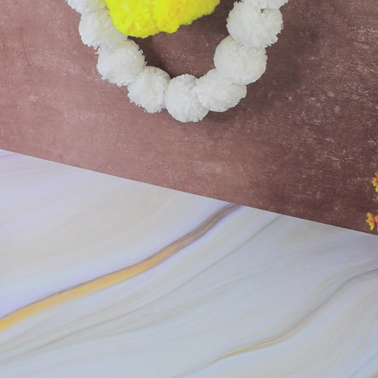 A partial view of a white and yellow floral garland on a brown and white marbled surface.