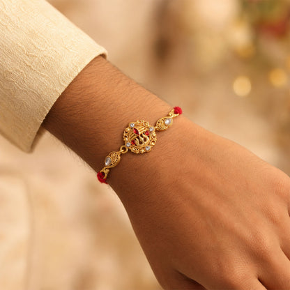 Gold-Toned Trishul Rakhi with Red Stones, Clear Crystal Accents & Designer Red Thread