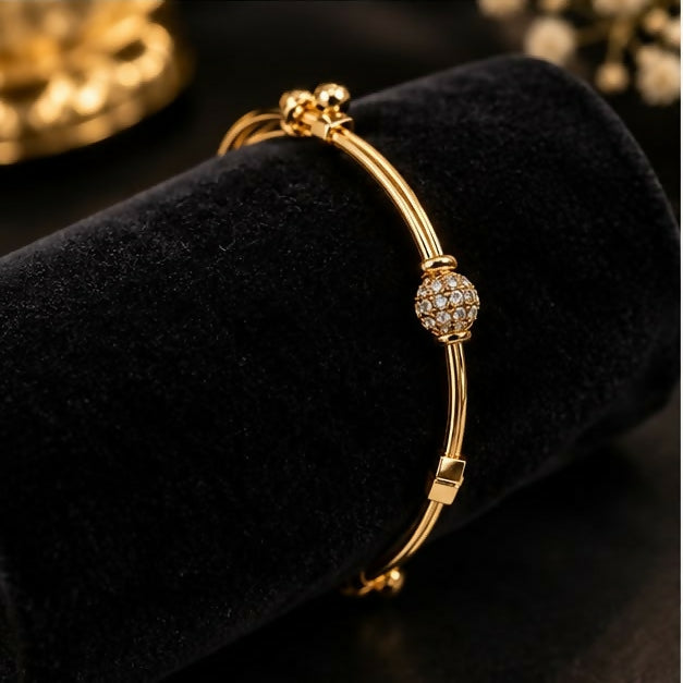 A gold-tone adjustable bangle bracelet with a brilliant crystal-studded sphere charm displayed on a black velvet cylinder.