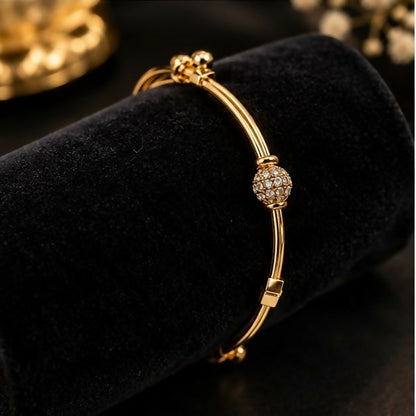 A gold-tone adjustable bangle bracelet with a brilliant crystal-studded sphere charm displayed on a black velvet cylinder.