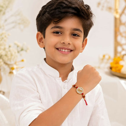 A young boy in a white shirt smiles at the camera, wearing the golden feather dial with crystal halo and rudraksha accents.