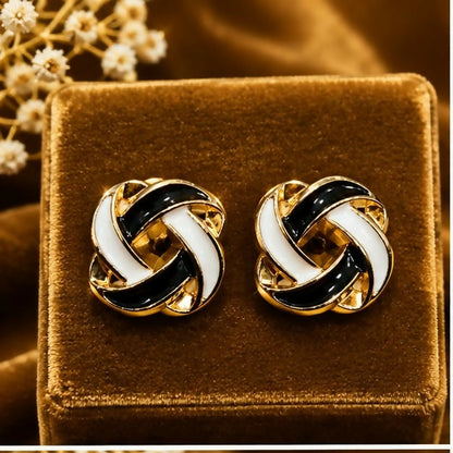 Two black and white enamel knot stud earrings are showcased on a brown velvet box.