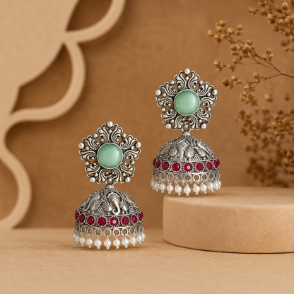 Oxidized silver jhumka earrings with mint green and ruby red stones on white background