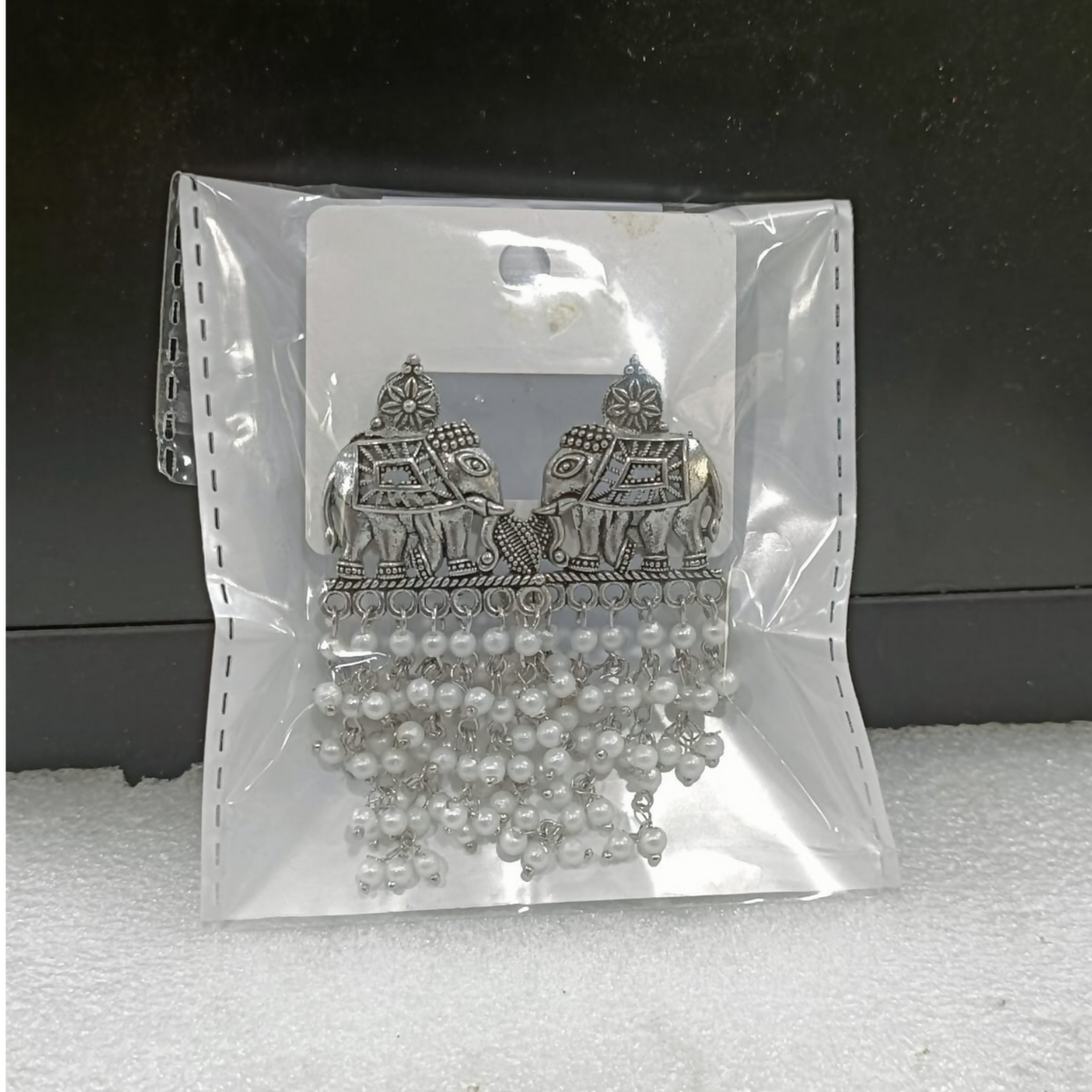 A pair of oxidized silver elephant earrings with white pearl drops sealed inside a clear plastic package.