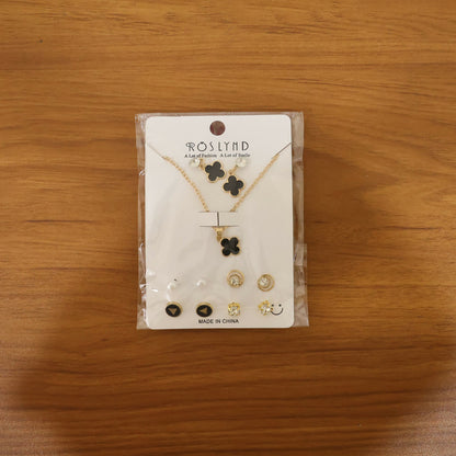Gold plated black clover pendant necklace and stud earrings set displayed on surface