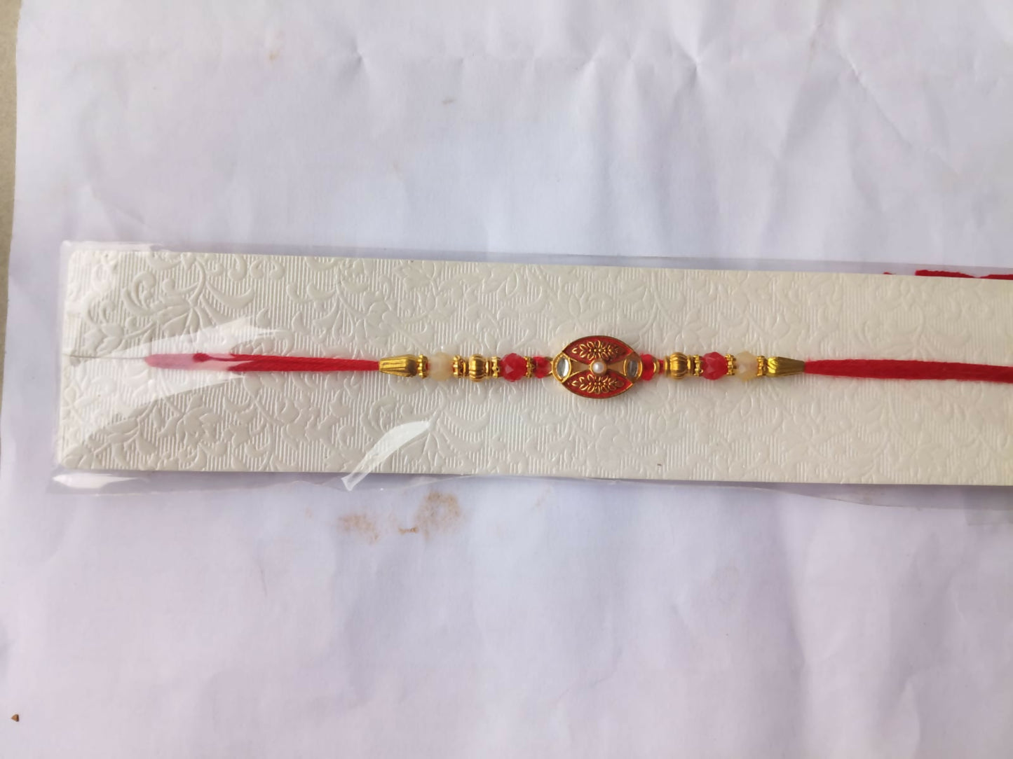 The red and gold beaded bracelet is packaged in a clear plastic sleeve on a white textured card.