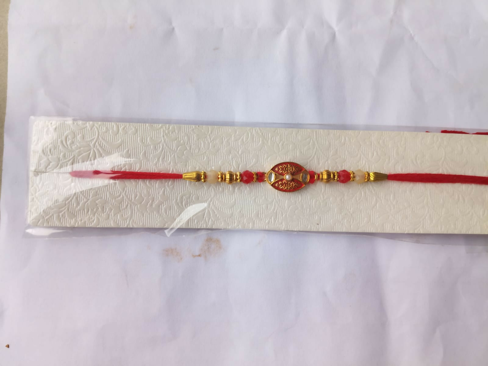 The red and gold beaded bracelet is packaged in a clear plastic sleeve on a white textured card.