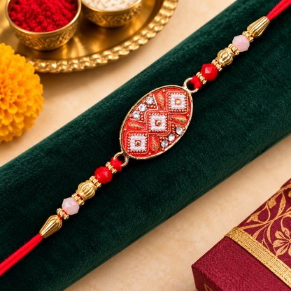 A red and gold Rakhi rests on a dark green velvet cloth, with a yellow flower and a small red gift box in the background.