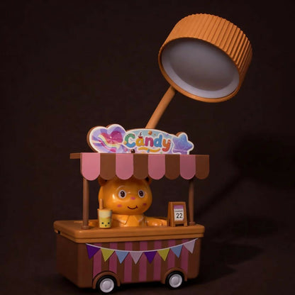 A brown and pink candy cart desk lamp with a glowing light, on a dark brown surface with a dark background.