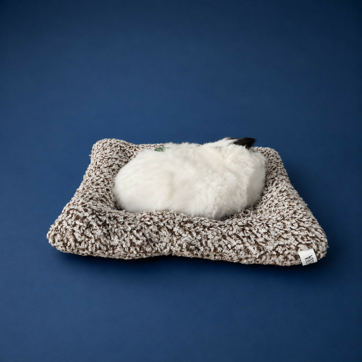 Sleeping cat plush toy resting peacefully on cushion base