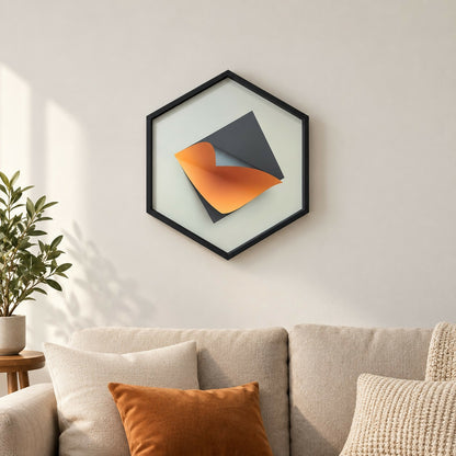 A black hexagon frame on a light wall contains a gray and orange abstract paper sculpture.